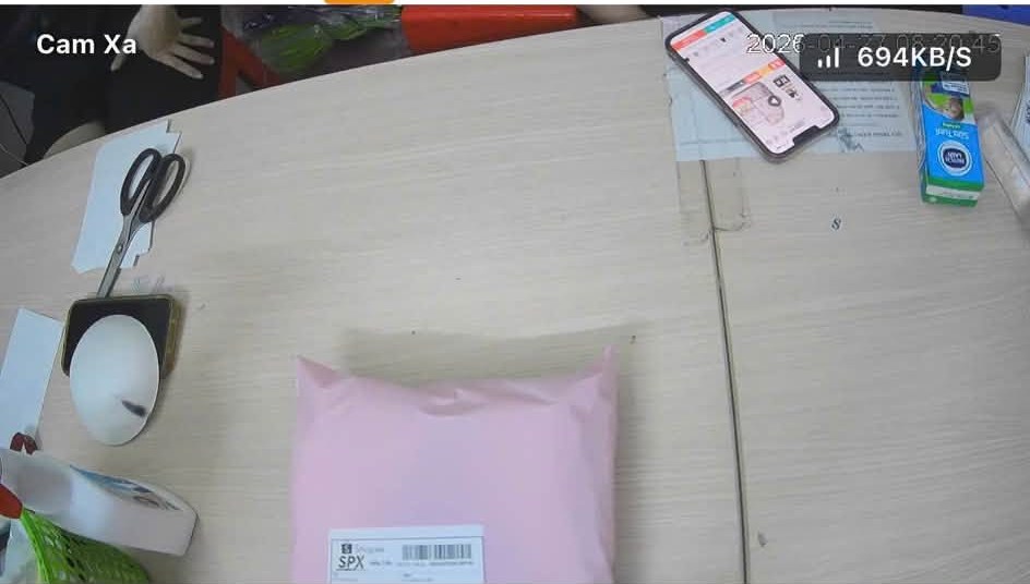 Khung hình camera đặt xa lấy toàn cảnh bàn đóng gói, thấy kiện hàng nhưng tem vận đơn quá nhỏ để đọc